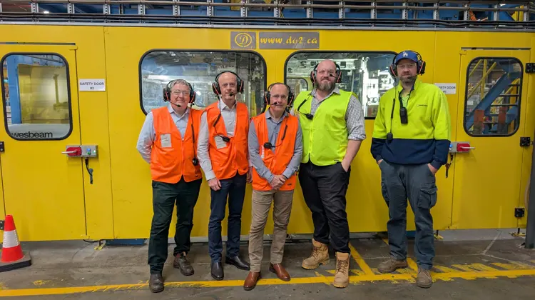 5 Men in high-vis standing in front of a yellow machine